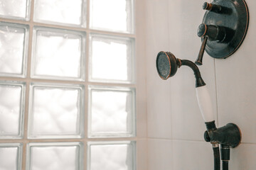 Close-up of a vintage shower handle with bronze finish and white ceramic detail, next to frosted...