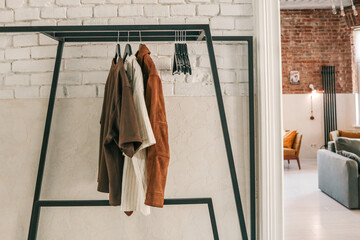 Set of neutral-toned shirts and a brown suede jacket hanging on a modern black clothing rack...