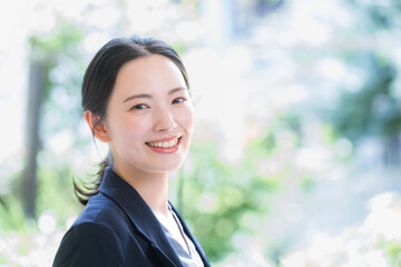 メインビジュアルにも綺麗な柔らかい新緑の中でパソコンを持つスーツの女性のカメラ目線ビジネスシーン　クローズアップ