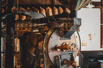 Industrial coffee roasting machine with brass handles and details, surrounded by shelves filled...