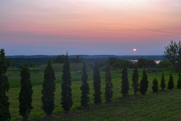 Meadow and trees against the background of the sun rising over the horizon on a summer morning. HDR photo.