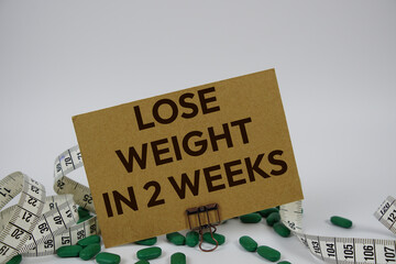 Lose Weight In 2 Weeks text with medicine, alarm clock and measuring tape on white background