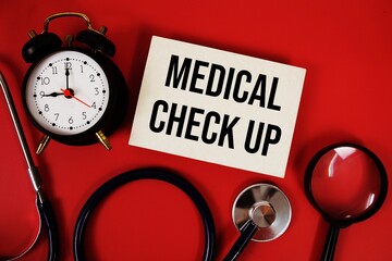 Medical Check Up text written on paper card with stethoscope, alarm clock and magnifying glass on...