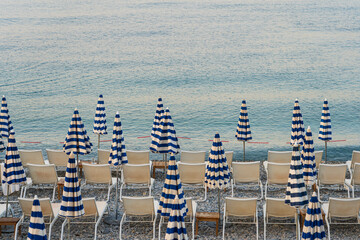 A calm scene on an empty pebble beach in Nice, France. Rows of sun loungers and the famous...