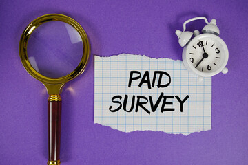 Paid Survey text written on paper with magnifying glass and alarm clock