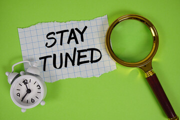 Stay Tuned text written on paper with magnifying glass and alarm clock