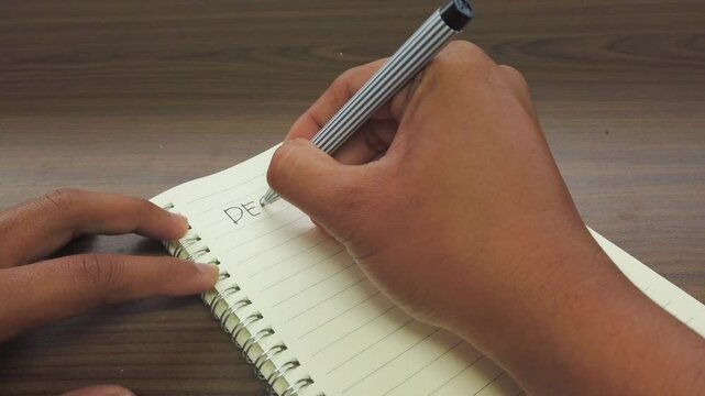 Hand of Asian Man writing December title on the notebook.