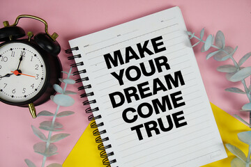 Make Your Dream Come True text written on notepad with alarm clock on pink background