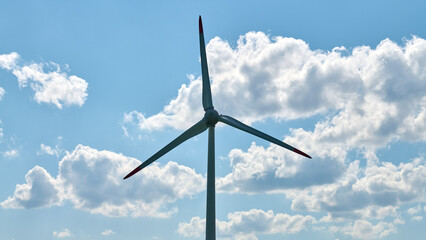 Silhouetted wind turbine set against clear blue sky with soft white clouds scattered across horizon, evoking serenity and power of innovation