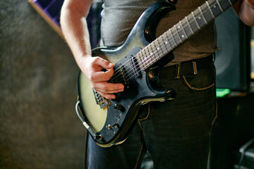 Musician playing an electric bass guitar at music rehearsal, practicing guitar technique in dimly...