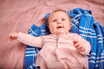 Baby girl with light brown hair, caucasian ethnicity, wearing pink dress, lies on blue blanket with...