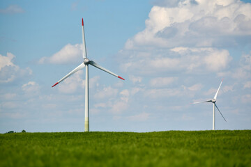 Wind turbine stands tall in lush green wheat field beneath bright blue sky with fluffy white clouds...