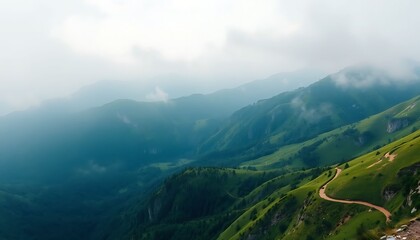 Fototapeta premium Drone view of a winding mountain road traversing lush green hills shrouded in morning mist.