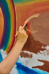 Young caucasian female uses paintbrush to create vibrant mural on outdoor wall. Scene captures...