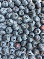 Close-up of fresh ripe blueberries scattered on a light surface. Natural organic fruit rich in antioxidants. Concept of healthy eating, freshness, and summer harvest. Bright natural lighting and minim
