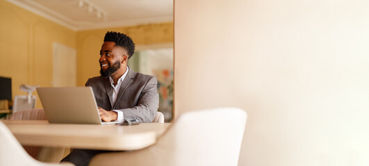 Smiling young businessman looking away confidently while working over wireless computer at desk in office