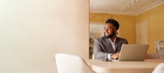 Male manager looking away and thinking business ideas while working over laptop at desk by wall in...
