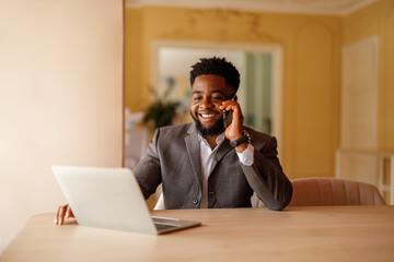 Portrait of confident male manager discussing project details over phone call while using laptop at...