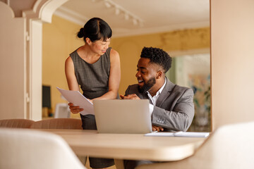 Businessman with laptop discussing financial reports with female manager at desk in corporate office