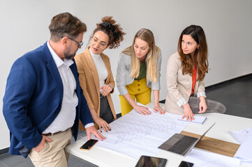 Male and female architects with blueprint on table discussing and planning new project in modern...