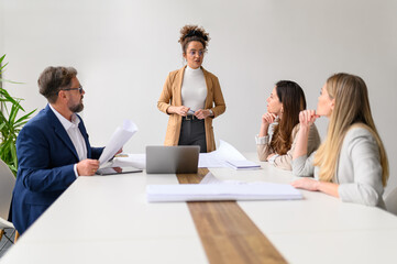 Confident businesswoman with blueprints on table discussing project plans with business colleagues...