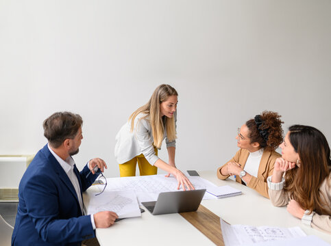 Female engineer reviewing blueprint with colleagues in meeting discussing construction plans and collaborating in office