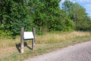 A interpretation signage panel in a country park, by a track with trees in the background....