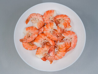 Boiled unshelled tails king prawns on dish on gray surface