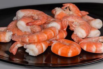 Boiled unshelled tails king prawns on black dish, front view