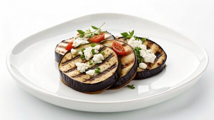 A delicious stack of grilled eggplant and tomato slices, artfully arranged and topped with crumbled feta cheese and fresh basil leaves, elegantly presented on a white plate.

