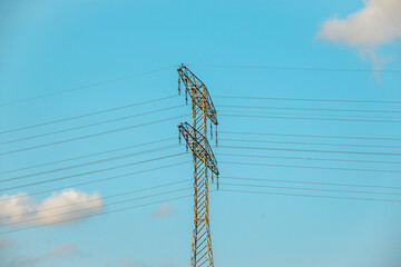 Two tall, black metal power lines stretch across a clear blue sky, with a few wispy clouds adding a...