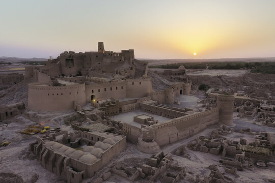 Aerial view of the ancient Arg-e Bam citadel glows with warm hues under the rising sun, its weathered walls telling tales of history, Bam, Kerman Province, Iran.
