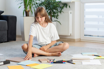 Preteen girl selecting notebook on floor. Preparing for school.