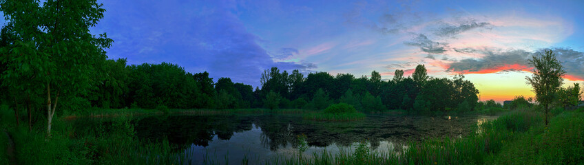 Panoramic view of a spectacular sunset over the lake and green park. The image was created in HDR style.