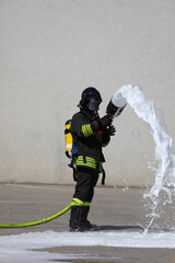 brave firefighter with big fire hose and white foam and protective helmet and breathing apparatus