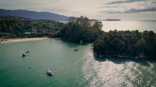 Aerial view of boats floating on the calm waters of the bay, panning along to the lush green landscape on Kaka Island, Kaiteriteri, Tasman Region, New Zealand.