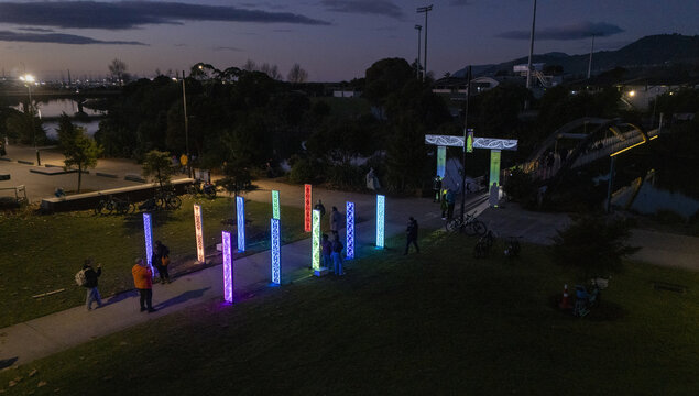 Aerial view of vibrant columns of light illuminating a park pathway near a bridge under a dusky sky, Nelson, Nelson Region, New Zealand.