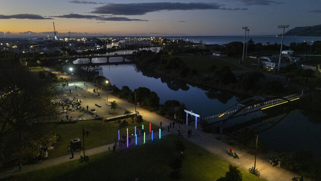 Aerial view of a tranquil river reflecting the city lights, with people strolling along pou rama,  illuminated pathways in the twilight, Nelson, Nelson Region, New Zealand.