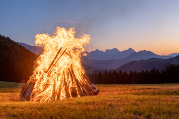 Solstice bonfire with sunset in the background in the Alps