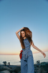 Lifestyle woman in modern boho-western denim street style dances freely by the ocean at sunset,...