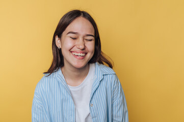 joyful young woman laughing with her eyes closed against a vibrant yellow background, capturing a...