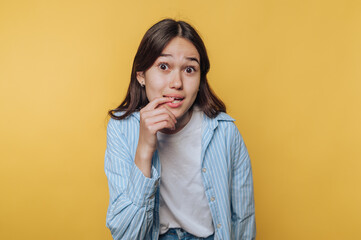 young woman playfully bites her lip, expressing a hint of shyness and curiosity  on vibrant yellow...