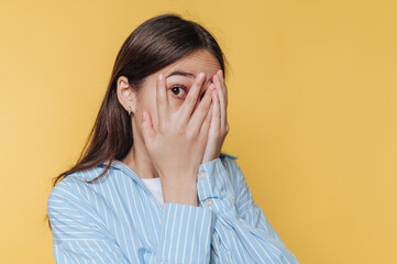 woman covers her face with her hands, expressing anxiety and discomfort on vibrant yellow background
