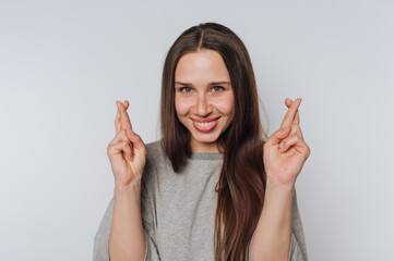 cheerful young woman smiles broadly with her fingers crossed, radiating optimism and positivity,...