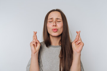 hopeful young woman crosses her fingers with closed eyes, embodying a desire for luck or a wish to...