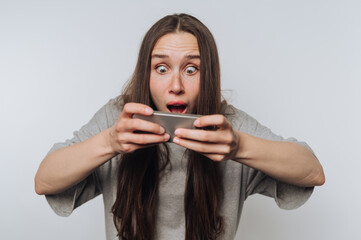 young woman expresses excitement while playing a mobile game on her smartphone on white background