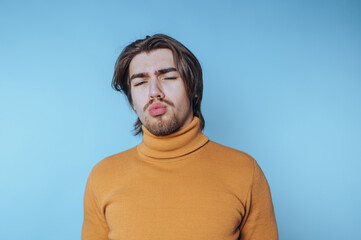 Obraz premium young man is seen wearing a turtleneck, eyes closed, portraying a moment of introspection and contemplation on blue background