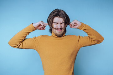 young man in a turtleneck playfully strains his features while pinching his ears, emanating a sense...