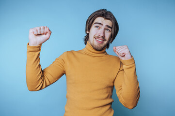 young man in a vibrant orange sweater exudes joy, celebrating with his arms raised in energy on...