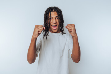 young man in a white t-shirt beams with excitement, raising his fists in triumph on white background